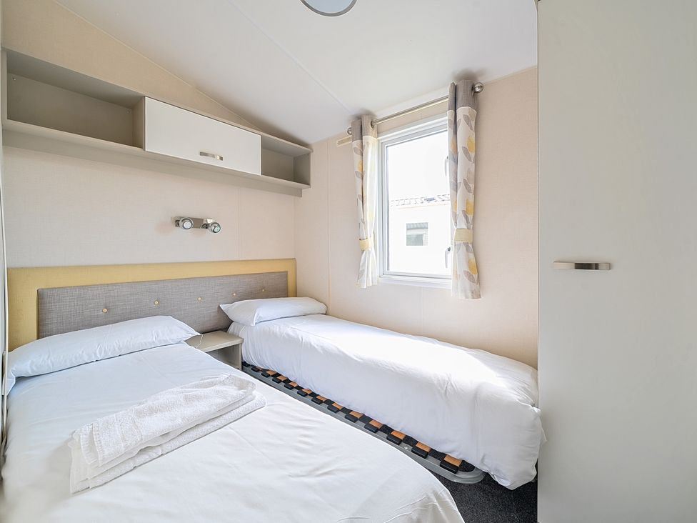 A bedroom with two single beds a window with curtains and overhead storage at Island Breeze - Hayling Island in Hayling Island Holiday Park