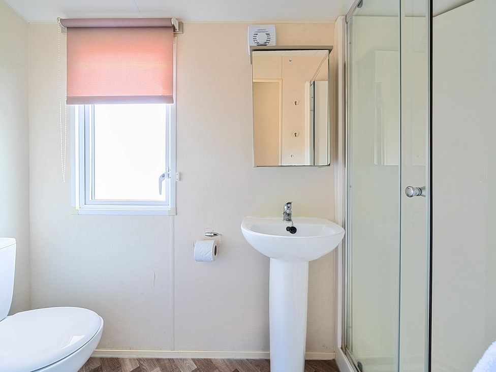 A bathroom with a toilet by a window with a pink blind a pedestal sink a mirrored cabinet and a glass shower enclosure at Island Breeze - Hayling Island in Hayling Island Holiday Park