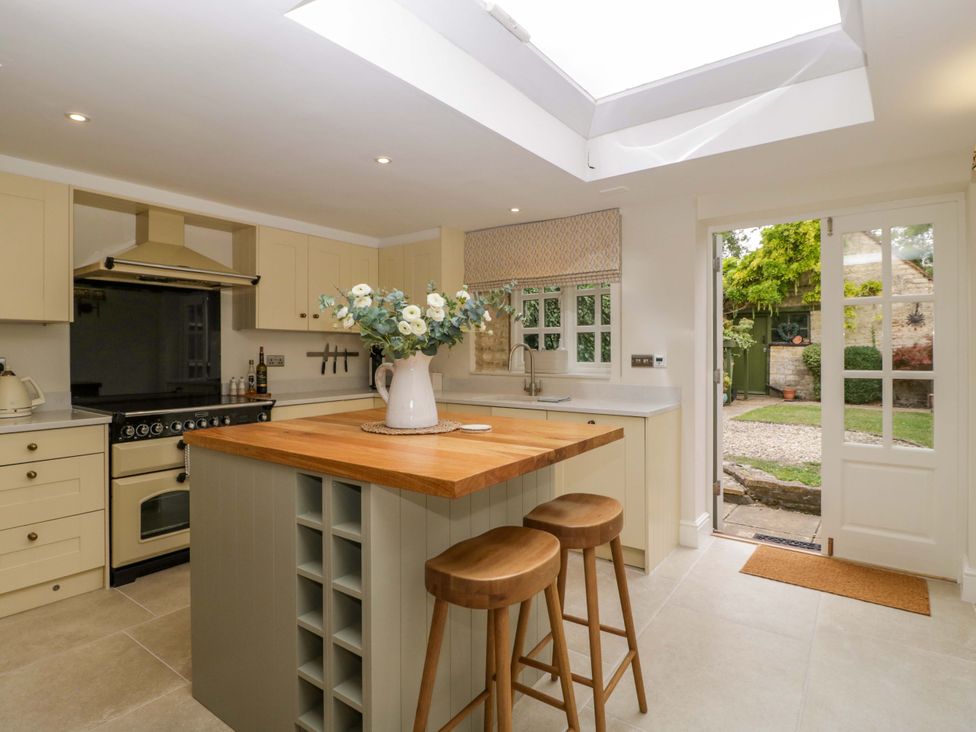 A kitchen with an island, stools, and a door opening to the garden at The Cottage in Stow-On-The-Wold