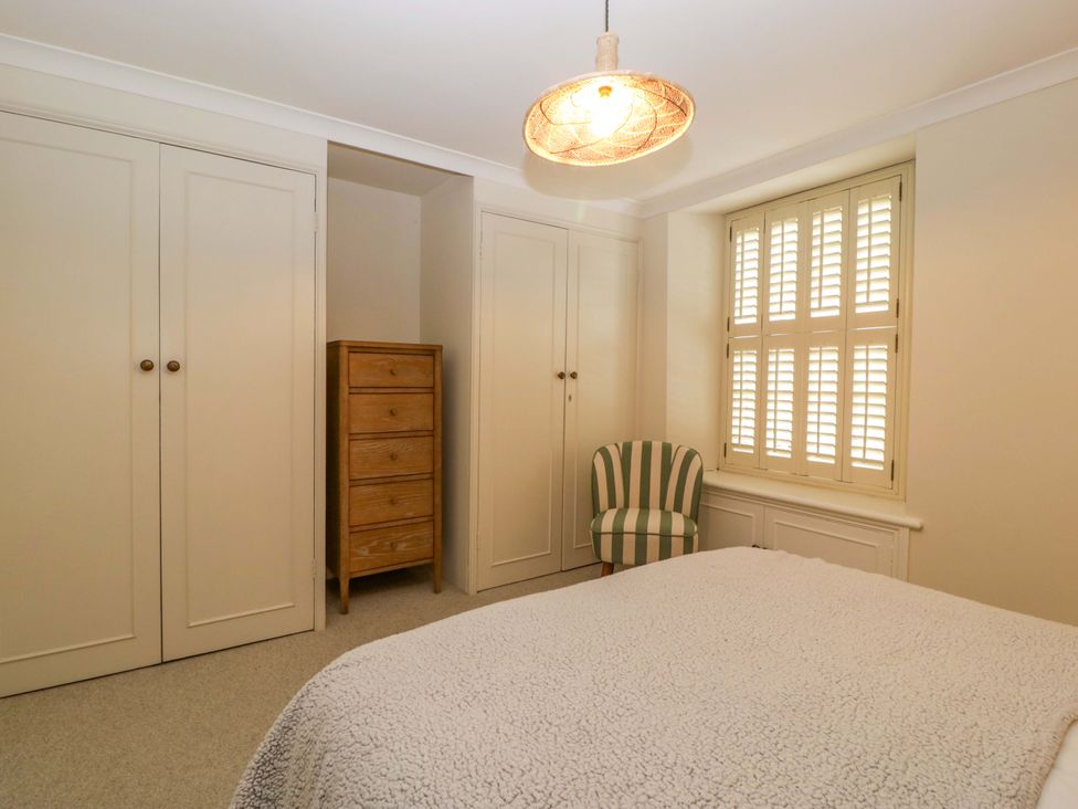 A bedroom with a bed, wardrobe, chest of drawers, and a chair at The Cottage in Stow-On-The-Wold