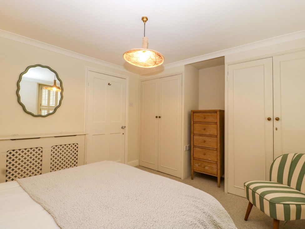 A bedroom with a bed, mirror, light fixture, chest of drawers, wardrobe, and chair at The Cottage in Stow-On-The-Wold