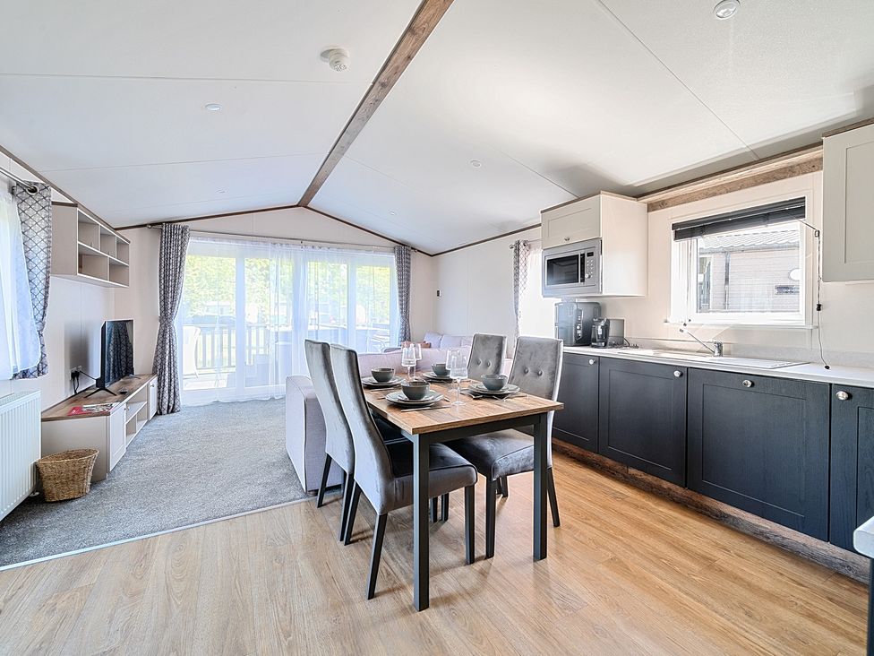 A kitchen and dining area with a table set for four and a living area with a television at Wave Whisperers - Hayling Island in Hayling Island Holiday Park