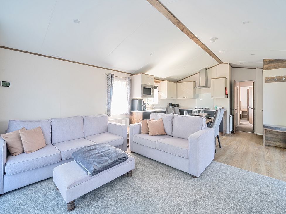 A living room with two sofas, an ottoman, and a kitchen with dining table and chairs at Wave Whisperers - Hayling Island in Hayling Island Holiday Park