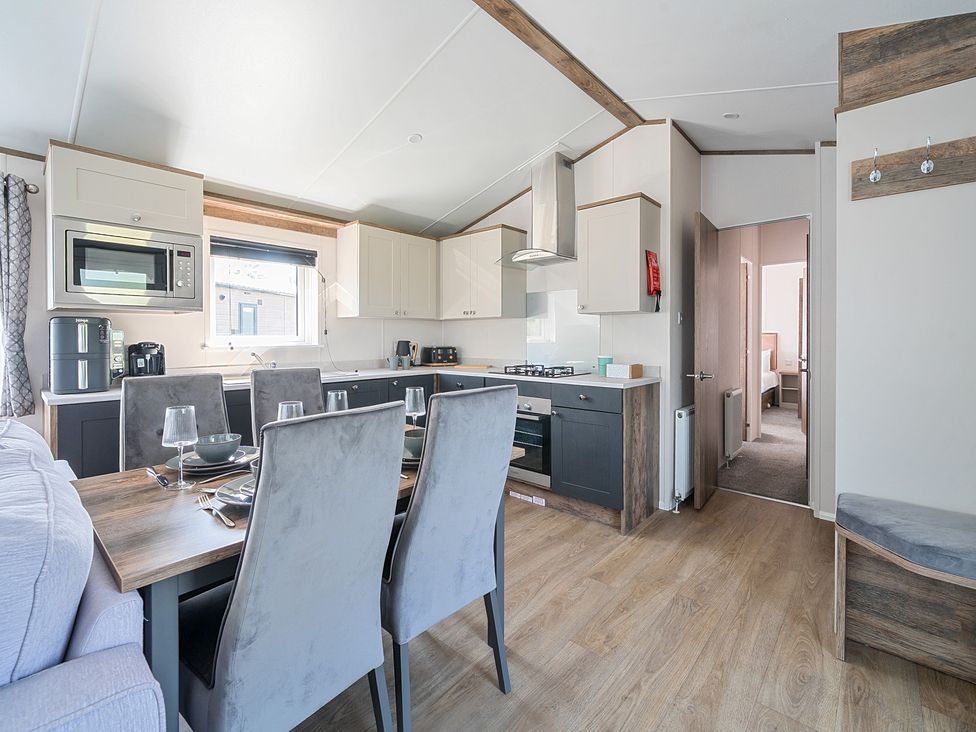 A kitchen with dining table and chairs next to a doorway showing a bedroom at Wave Whisperers - Hayling Island Holiday Park