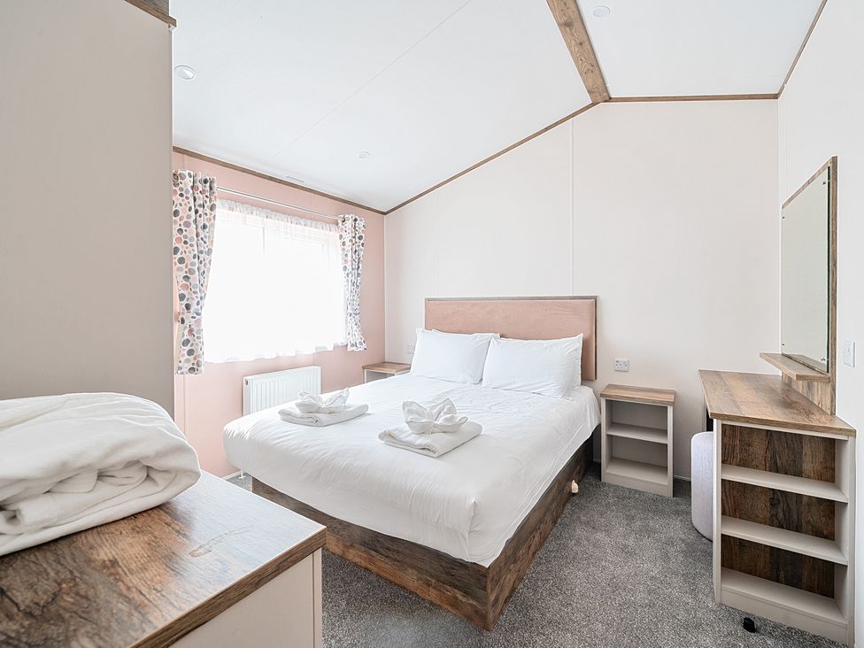 A bedroom with a double bed bedside tables curtains and a dresser at Wave Whisperers - Hayling Island Hayling Island Holiday Park