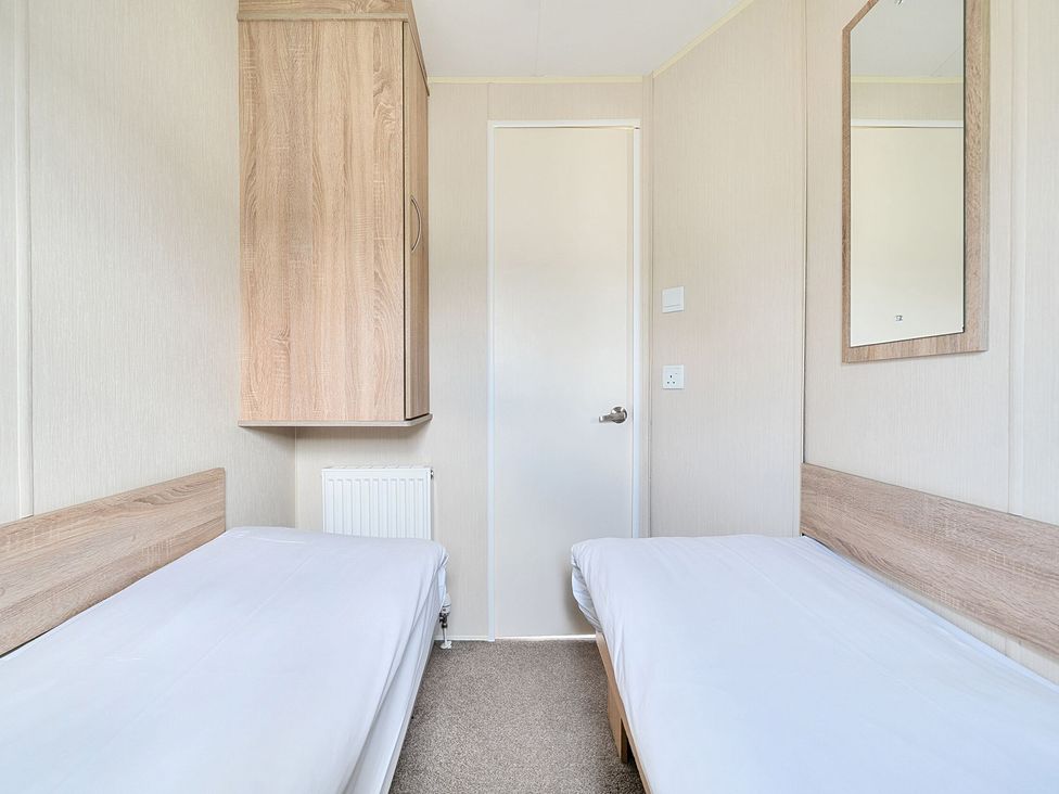 A small bedroom with two single beds a wall-mounted cabinet a radiator a door and a mirror at The Lookout - Hayling Island Hayling Island Holiday Park