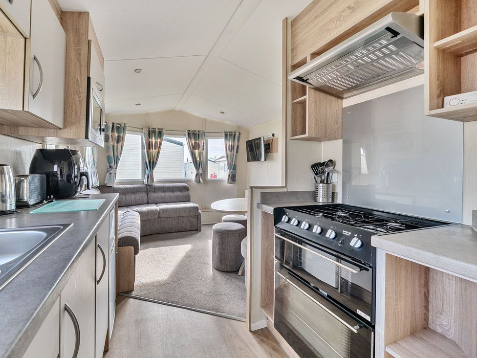A kitchen and living area with a stove microwave sofa and windows at The Lookout - Hayling Island in Hayling Island Holiday Park