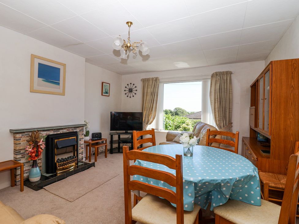 A living room with a blue polka dot tablecloth on a round dining table and a TV near a window at Ambermist in Churchstow