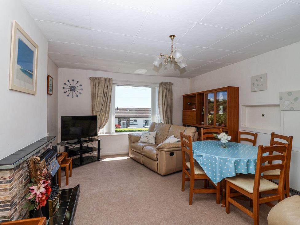 A living room with a beige sofa dining table with blue polka dot tablecloth and wooden chairs a television and cabinet at Ambermist Churchstow