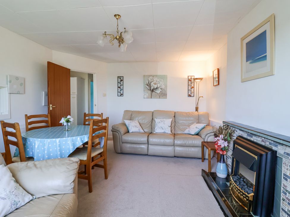 A living room with a beige sofa blue polka dot tablecloth on a dining table and a fireplace at Ambermist in Churchstow