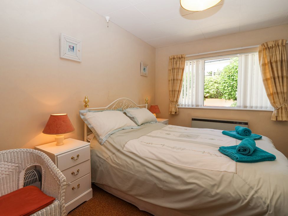 A bedroom with a double bed bedside tables with lamps a wicker chair and a window with curtains at Ambermist in Churchstow