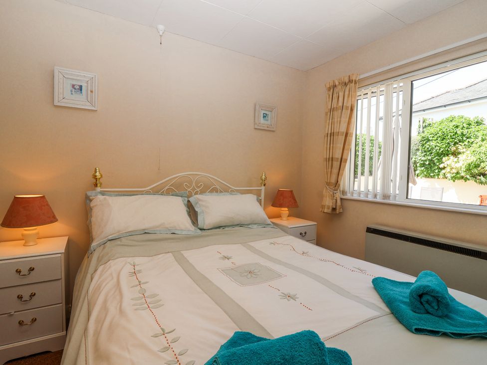 A bedroom with a double bed two bedside tables with lamps and a window with checkered curtains at Ambermist in Churchstow