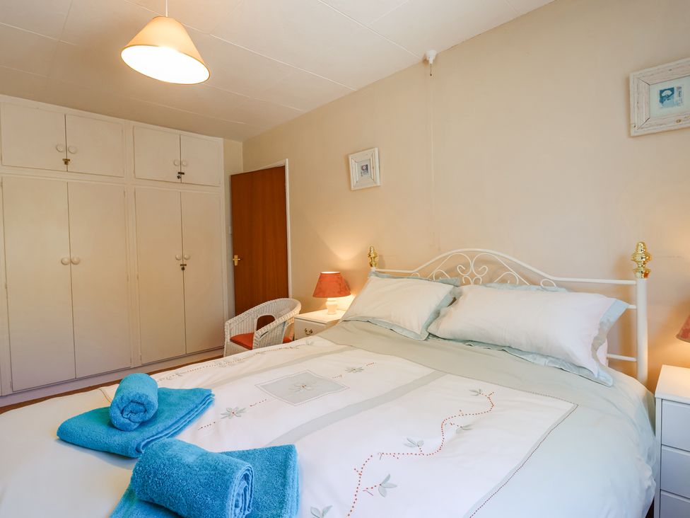 A bedroom with a double bed with blue towels on it bedside tables with lamps a wooden door and built-in wardrobes at Ambermist in Churchstow