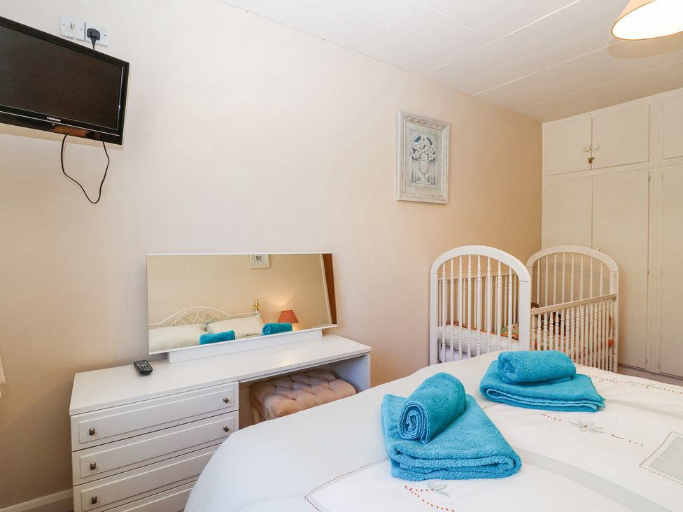 A bedroom with a bed featuring blue towels a white dresser with a mirror a white crib and a wall-mounted television at Ambermist in Churchstow