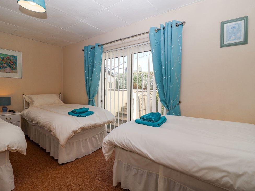 A bedroom with two single beds with white bedding and teal towels on each bed a bedside table with a lamp between the beds and a sliding glass door with teal curtains at Ambermist in Churchstow