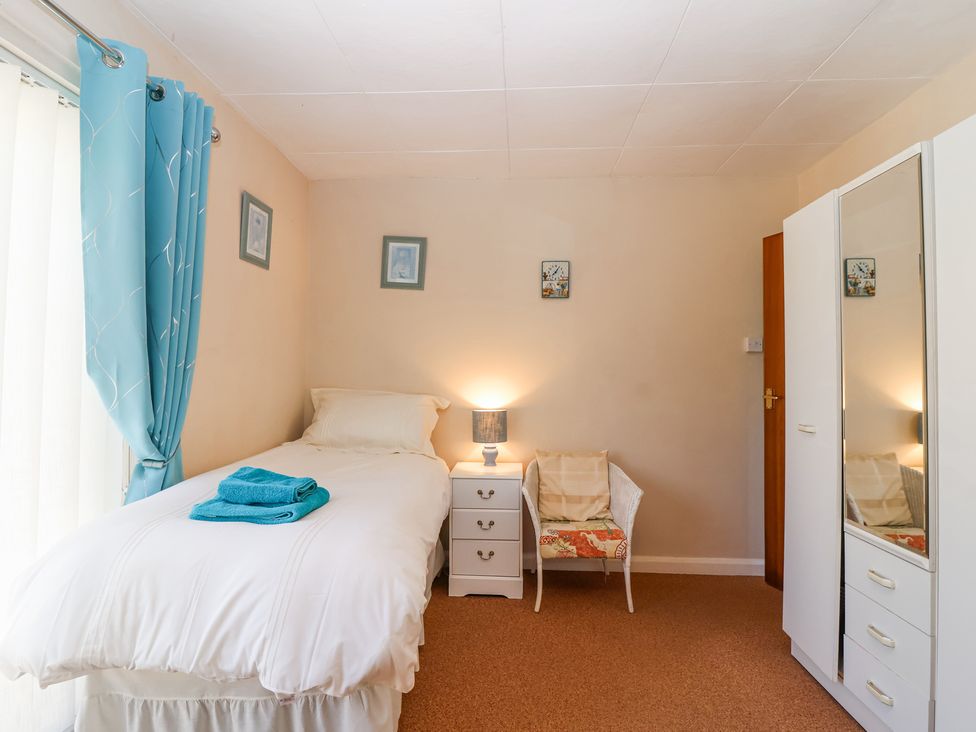 A bedroom with a single bed with blue towels on it a white nightstand with a lamp a white chair with cushions a white wardrobe with mirrored doors and blue curtains Ambermist Churchstow