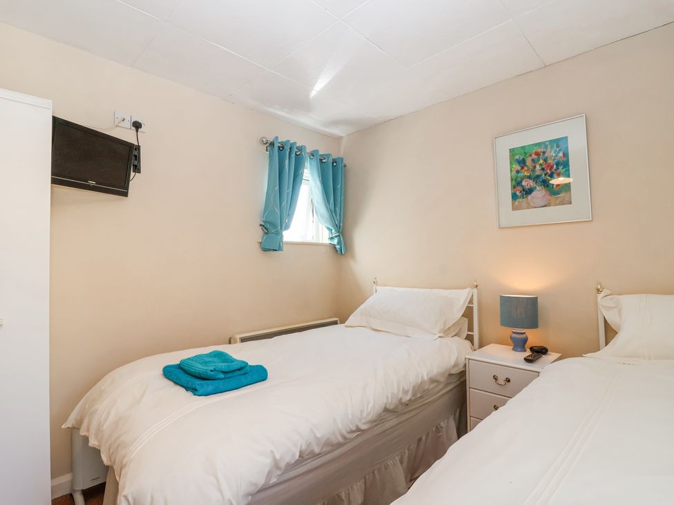 A bedroom with two single beds a nightstand with a lamp and a remote a wall-mounted tv and blue curtains at Ambermist in Churchstow