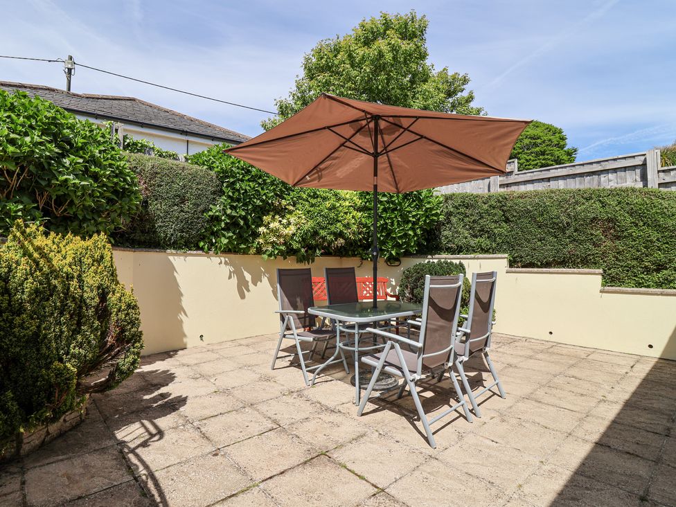 A patio with a table and four chairs under a large umbrella surrounded by green hedges at Ambermist in Churchstow