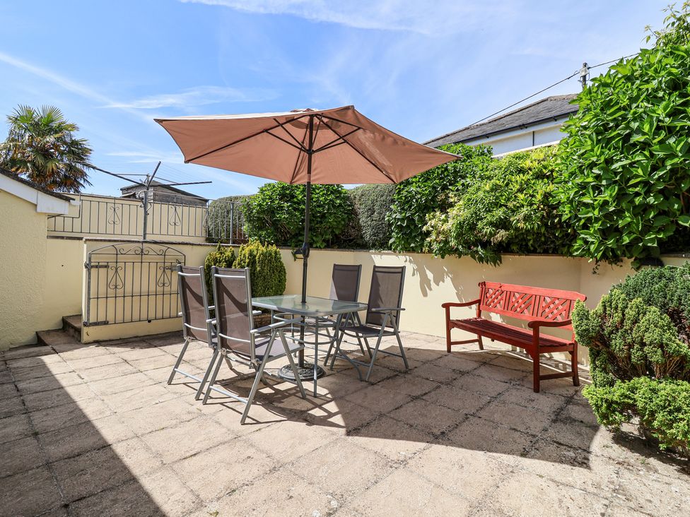 A patio with a glass table and four chairs under a large umbrella and a red bench against a wall at Ambermist in Churchstow