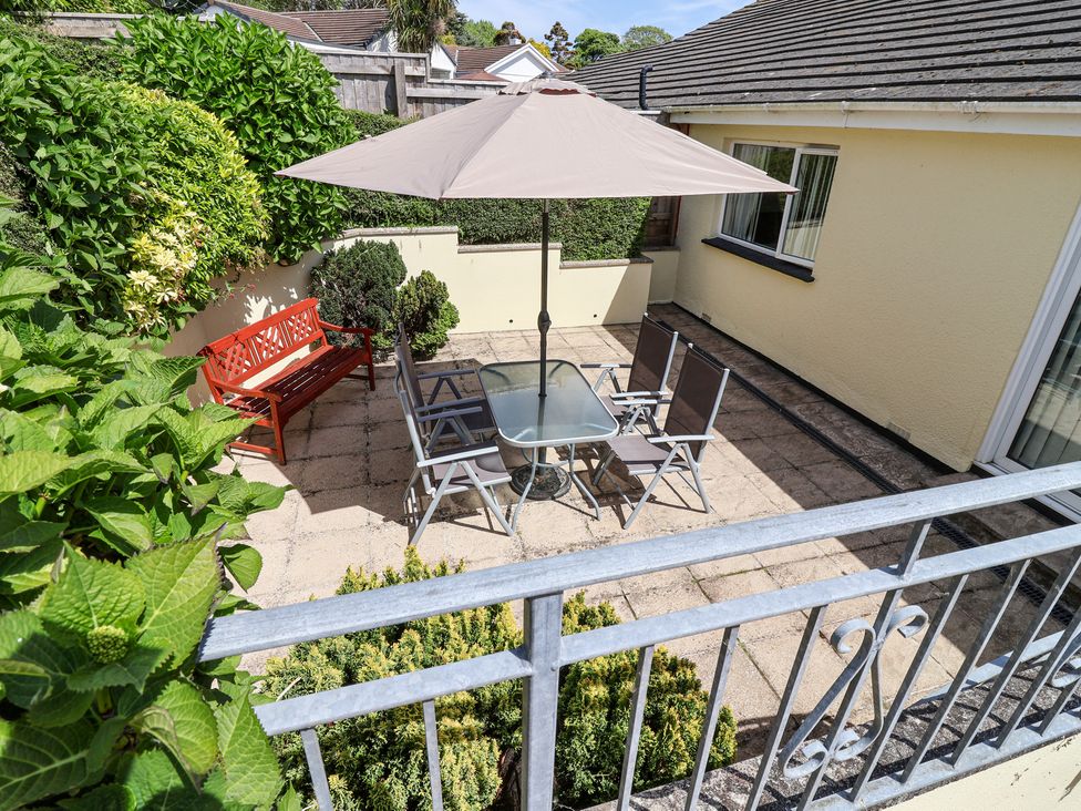 A patio area with a glass table and four chairs under a large umbrella a red bench and green plants at Ambermist in Churchstow