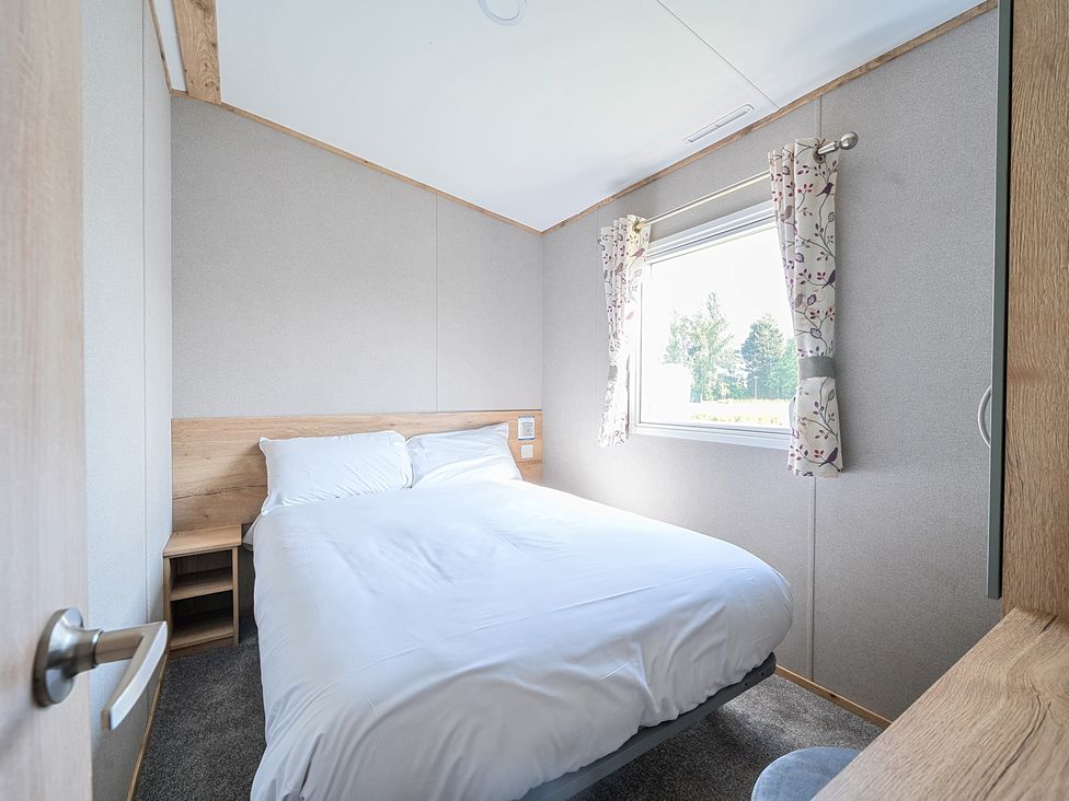 A bedroom with a double bed beside a window with curtains at Sunset Sands - Hayling Island in Hayling Island Holiday Park