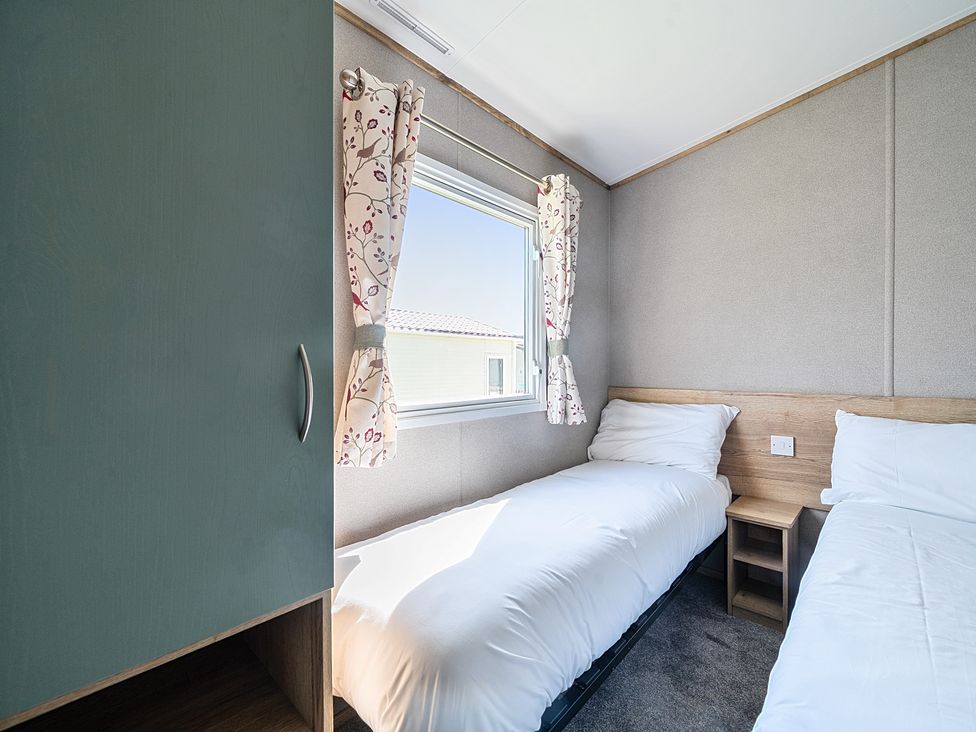 A bedroom with two single beds a window with floral curtains and a green wardrobe at Sunset Sands - Hayling Island in Hayling Island Holiday Park