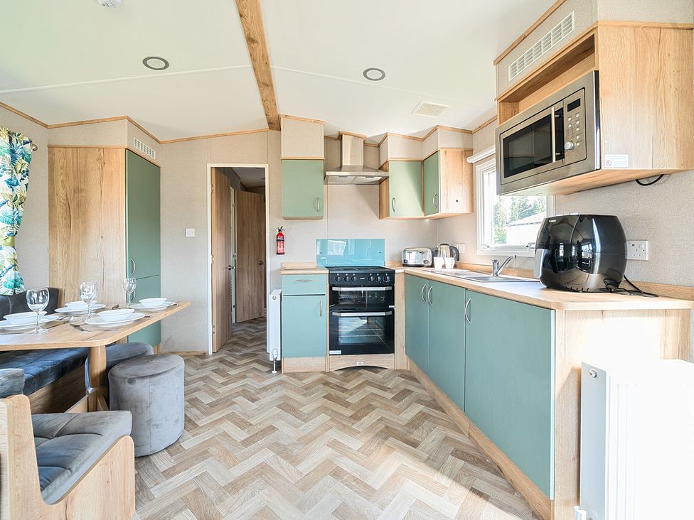 A kitchen with teal and wood cabinets a dining table with place settings and chairs at Sunset Sands - Hayling Island Hayling Island Holiday Park