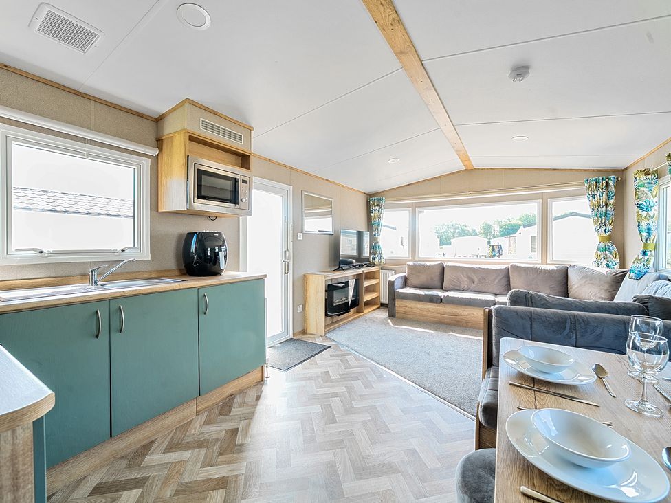 An open plan living space with kitchen cabinets microwave and air fryer a dining table set for two a TV and fireplace and sofas at Sunset Sands - Hayling Island in Hayling Island Holiday Park