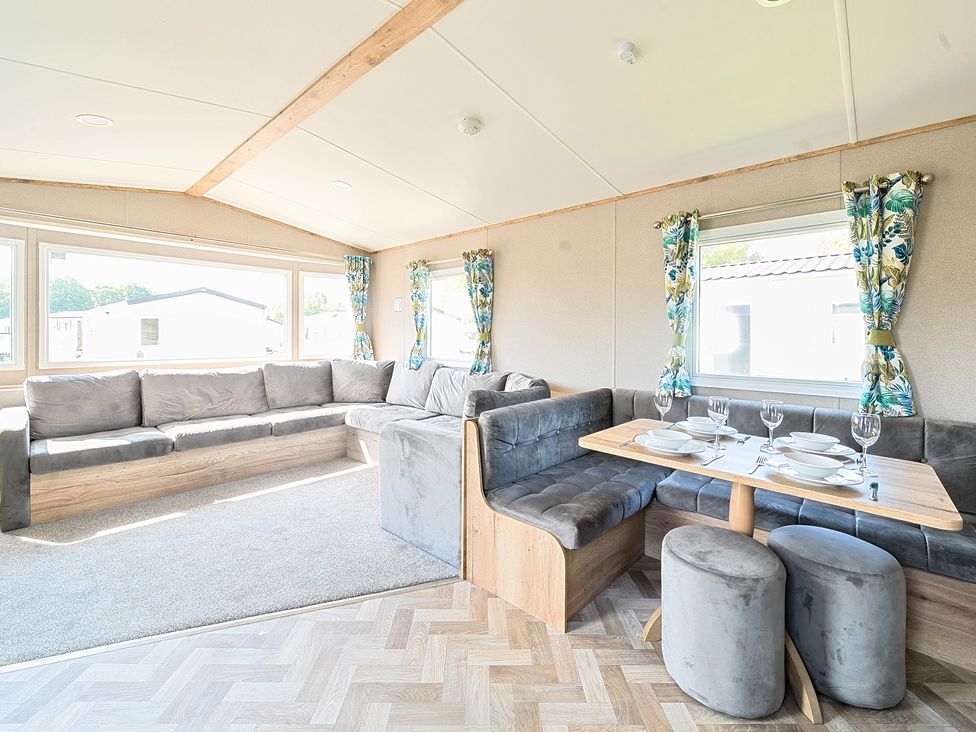 A living area with a grey sectional sofa and a dining table set with plates and glasses at Sunset Sands - Hayling Island in Hayling Island Holiday Park