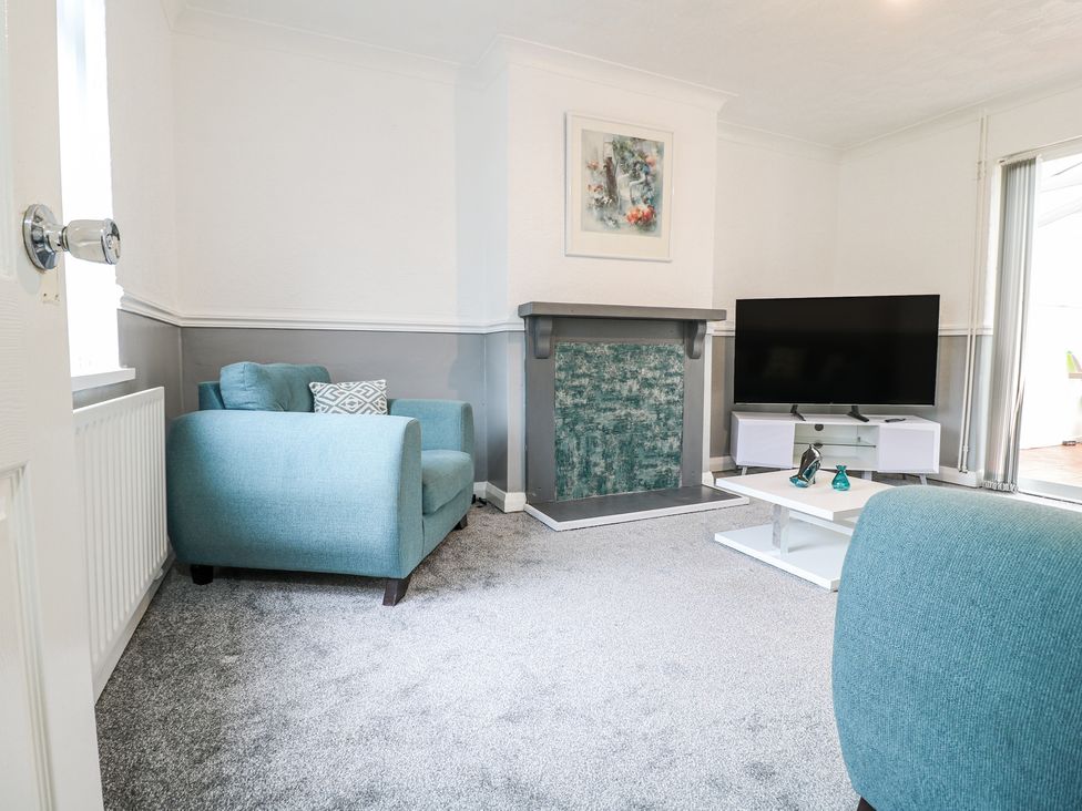 A living room with two blue armchairs a fireplace a television on a white stand and a white coffee table at 46 Dalby Road in Antsey