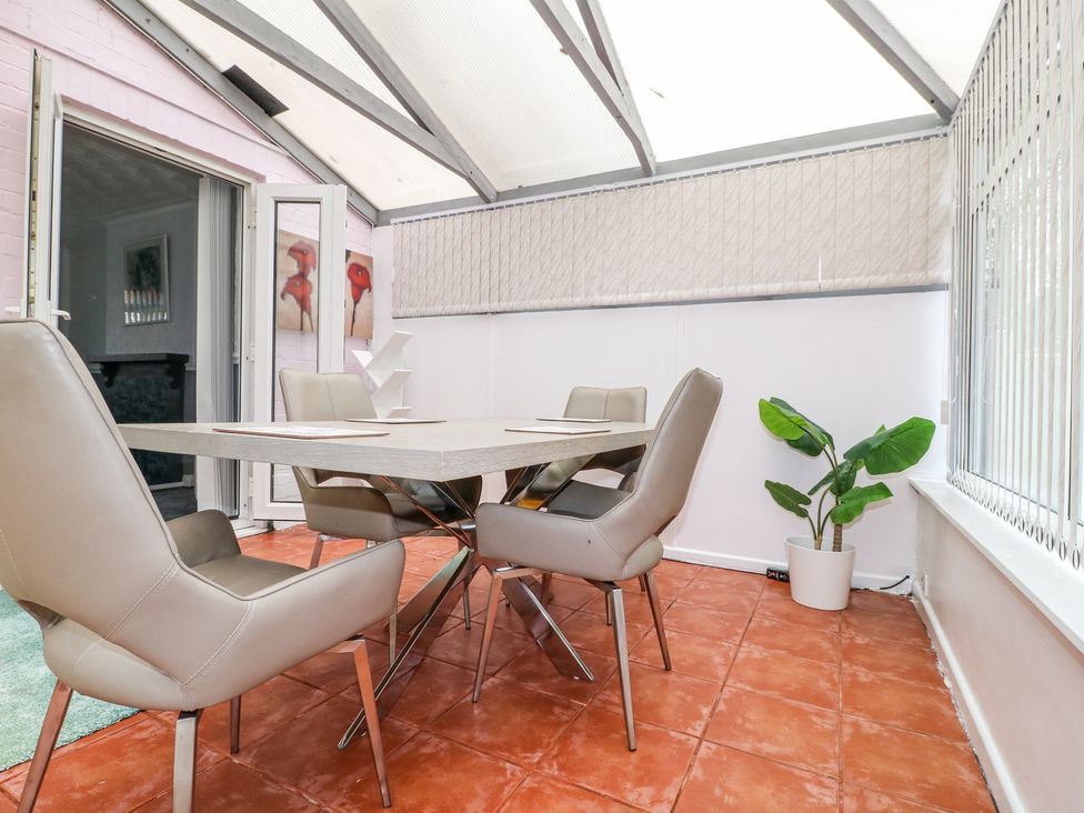 A dining area with a table and four chairs a potted plant on a tiled floor in a room with large windows at 46 Dalby Road in Antsey