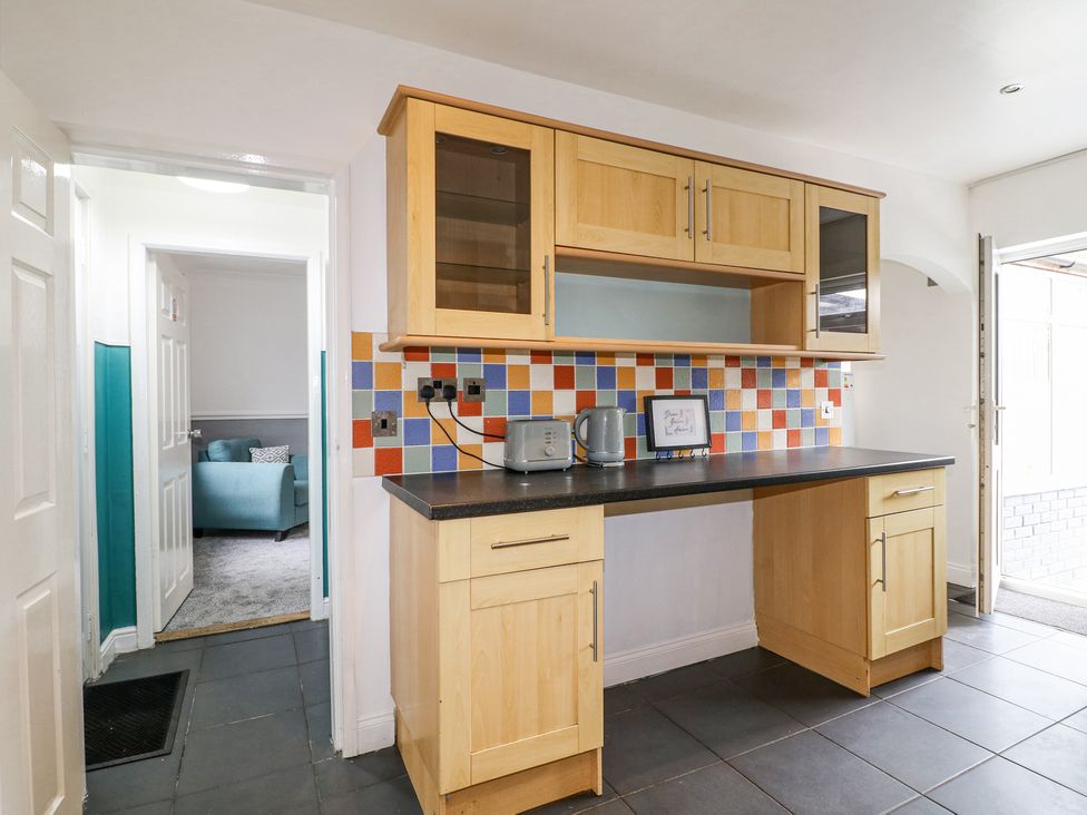 A kitchen with wooden cabinets a black countertop a colorful tiled backsplash a toaster a kettle and a framed picture at 46 Dalby Road Antsey