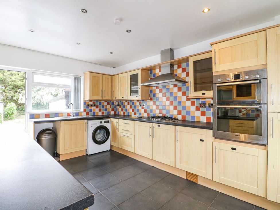 A kitchen with wooden cabinets multicolored tiled backsplash black countertops a washing machine and built in double oven at 46 Dalby Road in Antsey