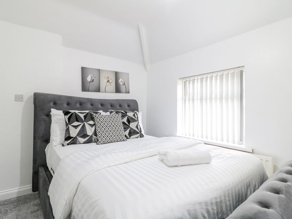 A bedroom with a bed with geometric patterned pillows and a window with vertical blinds at 46 Dalby Road in Antsey
