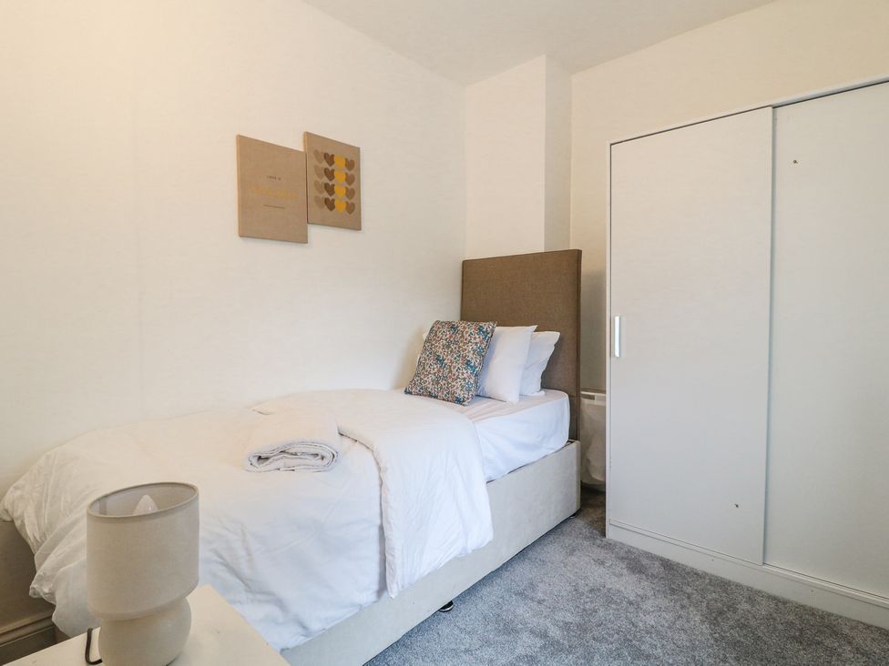 A bedroom with a single bed white bedding a floral cushion a bedside table with lamp and a white wardrobe at 46 Dalby Road in Antsey