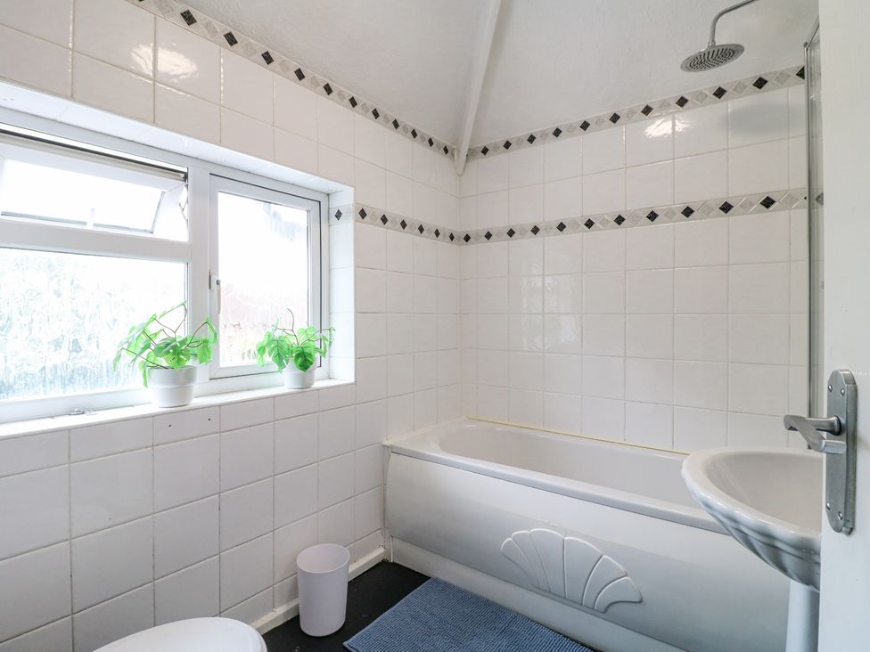 A bathroom with a bathtub sink window two plants and a trash bin at 46 Dalby Road Antsey