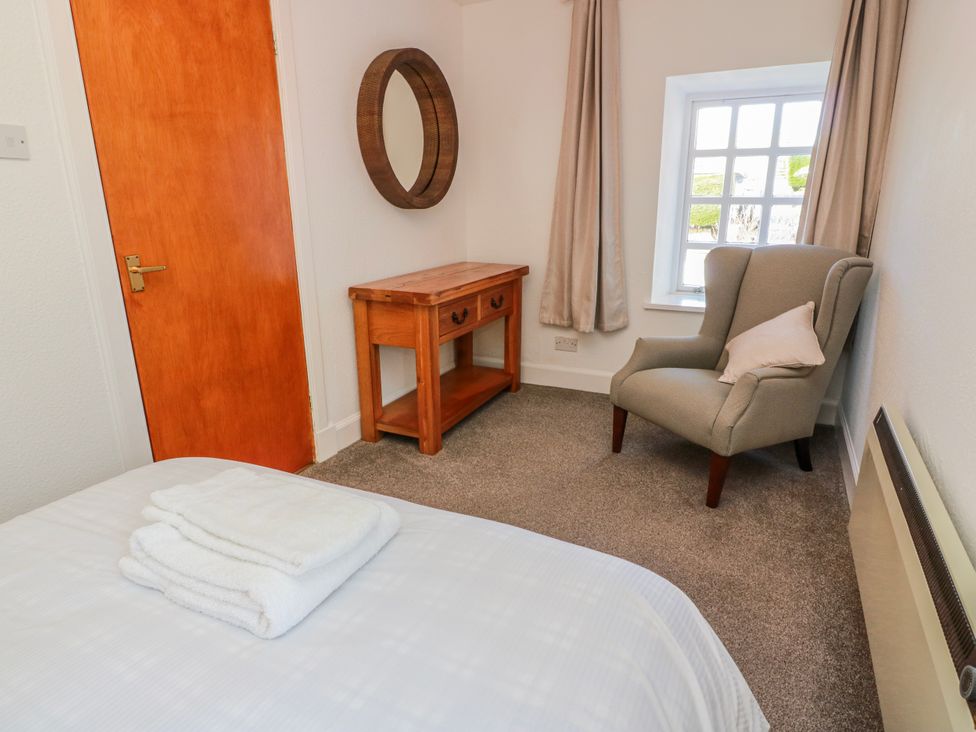 A bedroom with a bed, towels, table, mirror and chair at The Old Coach House in Lockerbie