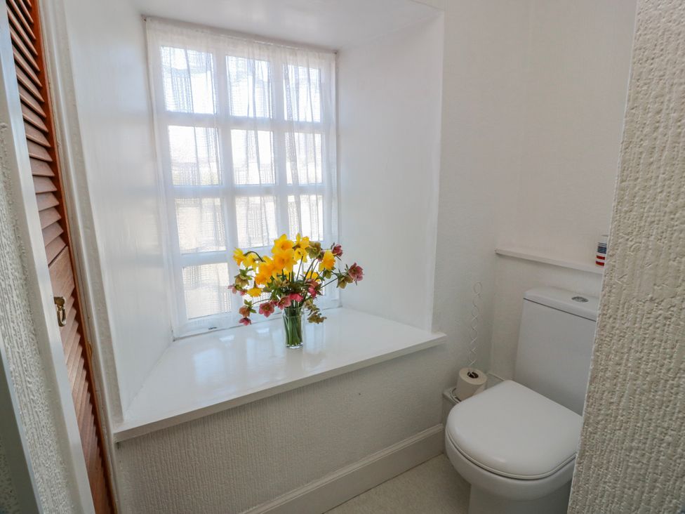 A bathroom with a toilet and flowers on a shelf at The Old Coach House Lockerbie