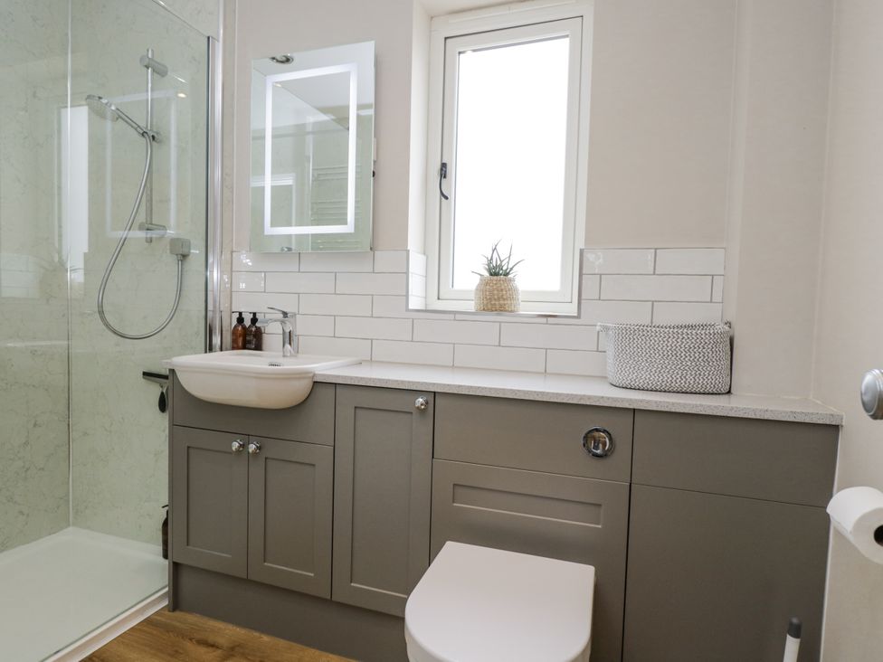 A bathroom with a shower, toilet, sink, and mirror at Hayloft
