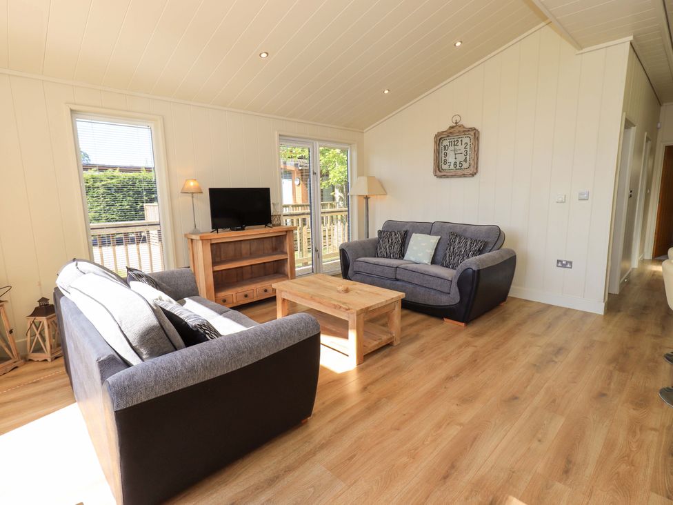 A living room with two sofas a wooden coffee table a television on a stand and large windows at Kingfisher Lodge in Gargrave