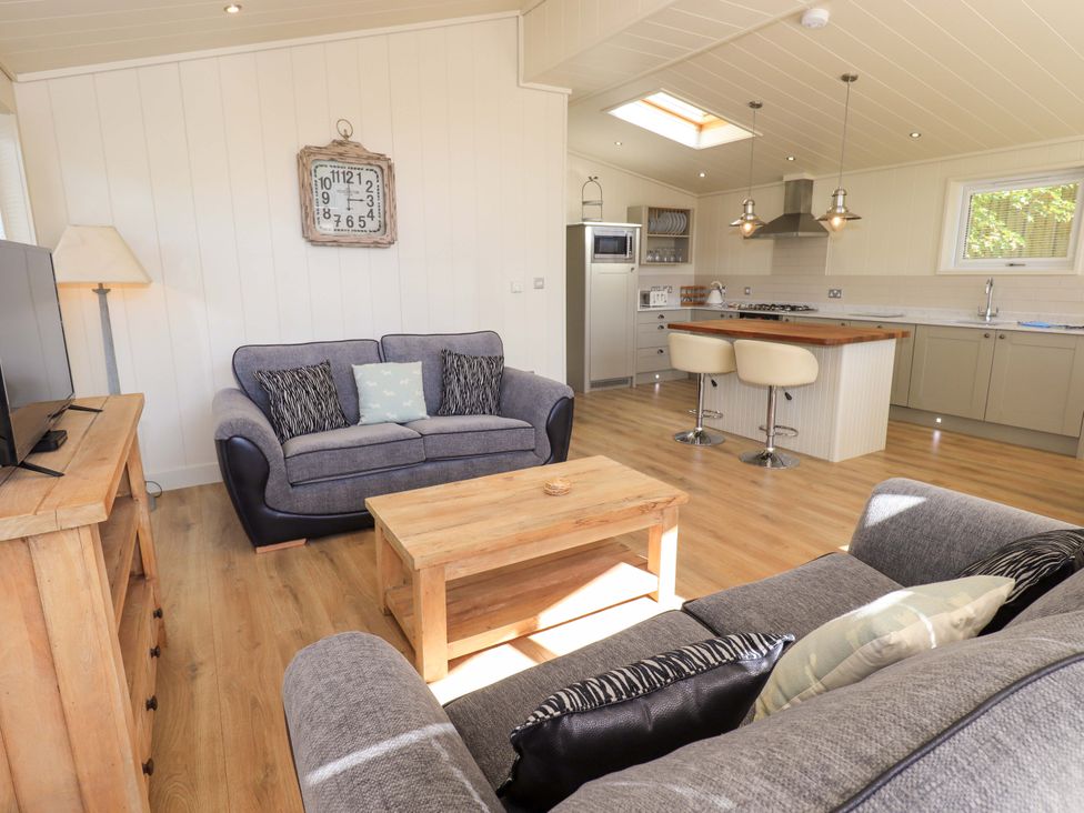 An open living room and kitchen area with gray couches a wooden coffee table and kitchen island at Kingfisher Lodge in Gargrave