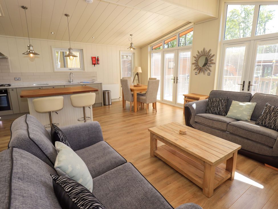 An open living space with two sofas facing a wooden coffee table and a dining table with chairs near large windows at Kingfisher Lodge in Gargrave