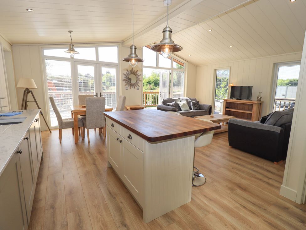 A combined kitchen and living room with a wooden island a dining table sofas and a television at Kingfisher Lodge in Gargrave