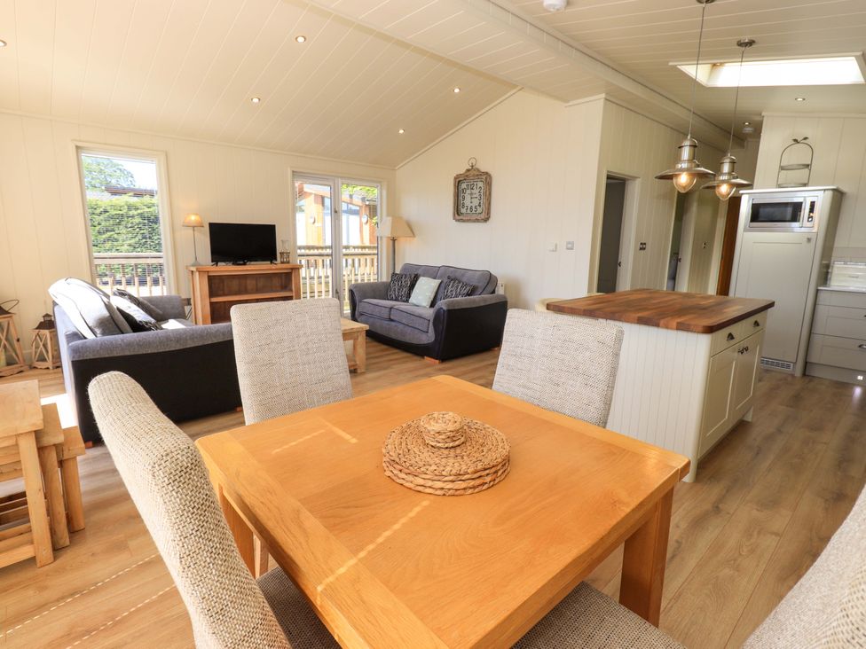 A living room and kitchen area with a wooden dining table and chairs a kitchen island and two sofas at Kingfisher Lodge in Gargrave