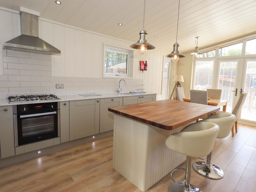 A kitchen with an island and two stools a dining table with chairs and large windows at Kingfisher Lodge in Gargrave