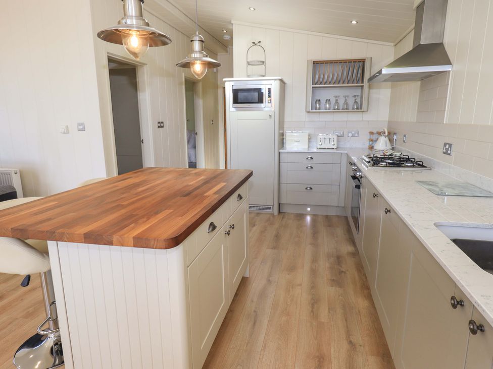 A kitchen with a wooden island countertop a stove sink microwave and cabinets at Kingfisher Lodge in Gargrave