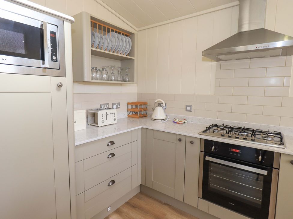 A kitchen corner with a microwave oven plates glasses a toaster a kettle and a gas stove with an oven at Kingfisher Lodge in Gargrave