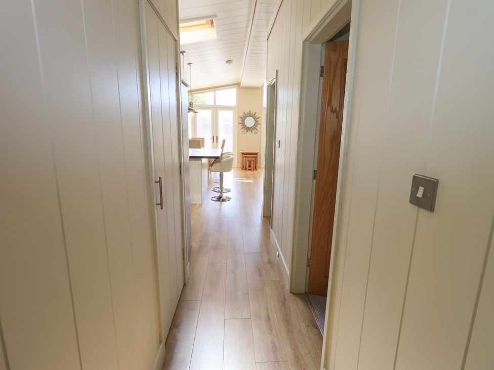 A hallway with wooden floor leading to a dining area with chairs and a mirror on the wall at Kingfisher Lodge in Gargrave