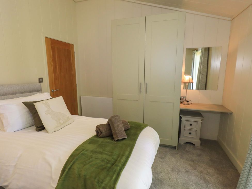 A bedroom with a bed, wardrobe, desk with lamp and mirror at Kingfisher Lodge in Gargrave
