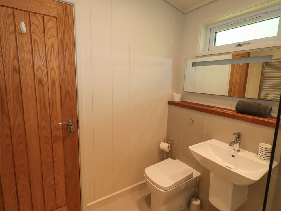 A bathroom with a wooden door toilet sink mirror and towel at Kingfisher Lodge in Gargrave